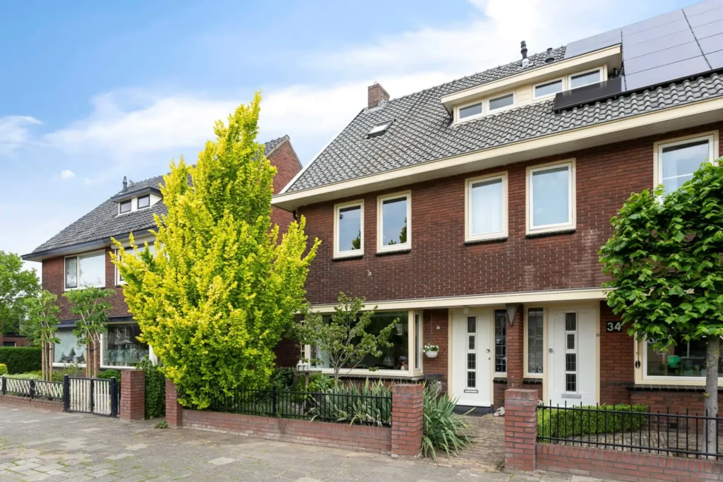 Bakstenen twee-onder-een-kapwoning met voortuin en hek, onder een blauwe lucht